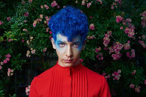 human blue haired man standing in front of pink flower plants person