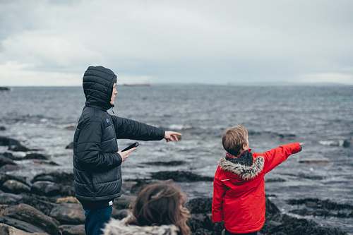 person boy and man pointing on sea taken under white clouds during daytime human