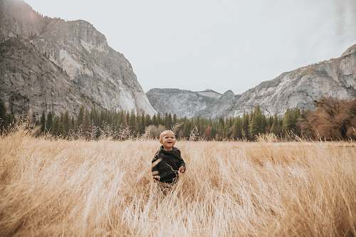 grass boy in black jacket stand on brown grass near mountain human