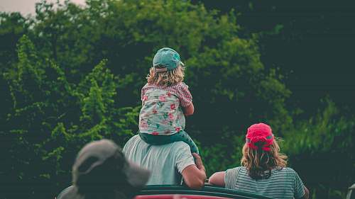 person girl riding man's shoulder beside girl near trees during day human