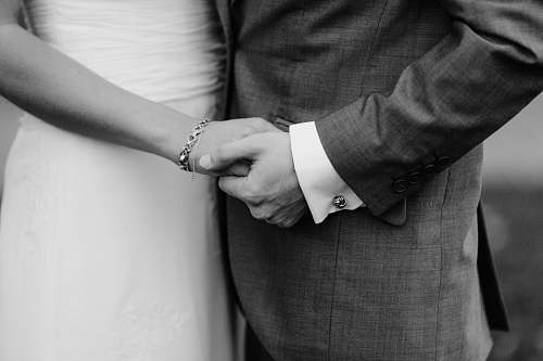human grayscale photo of man and woman holding each others hands black-and-white