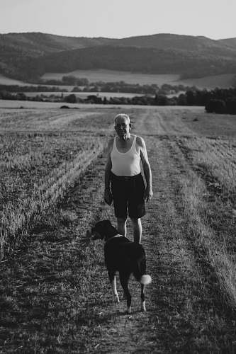 human grayscale photo of man standing beside adult short-coated dog black-and-white