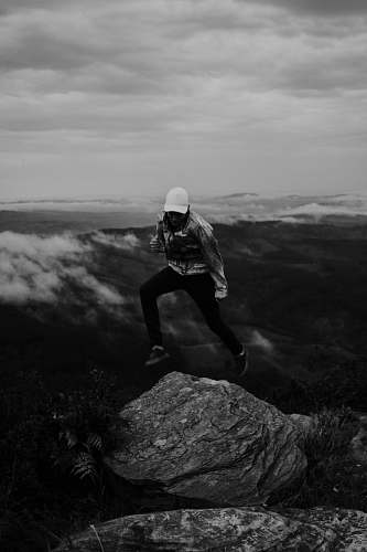 person grayscale photo of person jumping on rock black-and-white