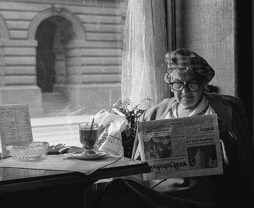 black-and-white grayscale photo of woman sitting while reading newspaper newspaper