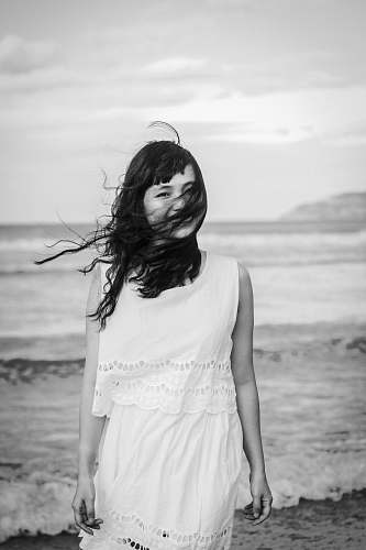 person grayscale photography of woman standing on seashore black-and-white