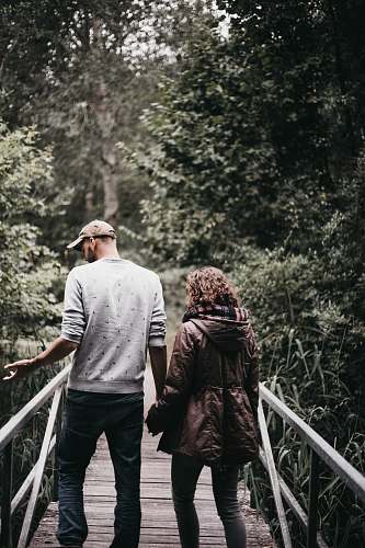 human man and woman holding hands walking on bridge during daytime person
