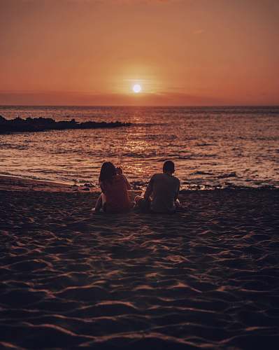 human man and woman sitting on beach during golden hour person