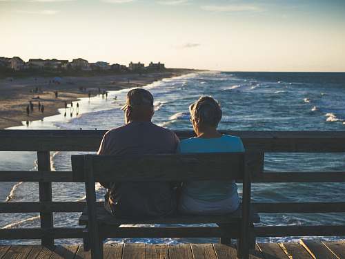 human man and woman sitting on bench in front of beach person