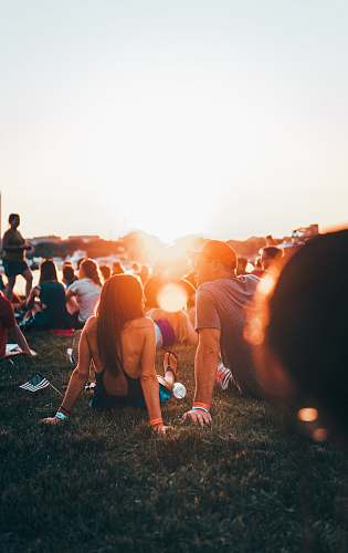 person man and woman sitting on grass surrounded with people during golden hour human