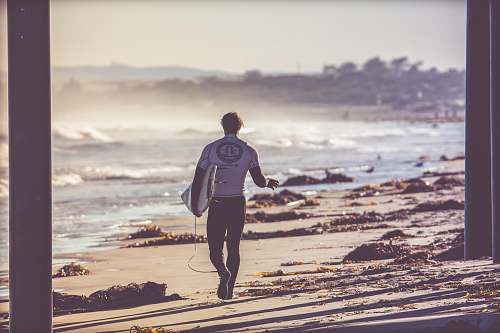 person man carrying white surfboard walking towards beach human