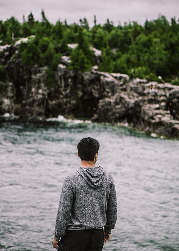 human man facing backward fronting body of water and trees foliage person
