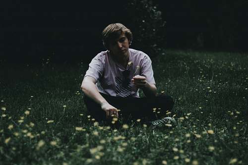 human man holding flower while sitting on green grass field person