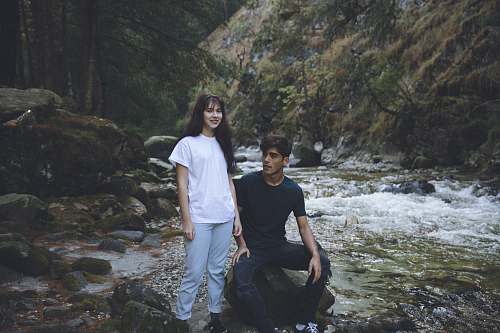 person man in blue shirt sitting beside woman in white shirt standing on river human