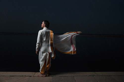 person man in white and brown traditional dress standing beside black wall human