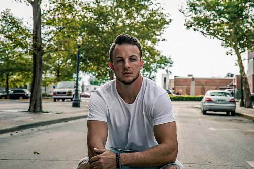 human man sitting in the middle of road with two grey cars on background car