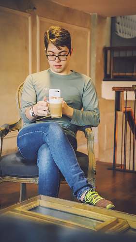 human man sitting on brown armchair while taking photo of a cup person