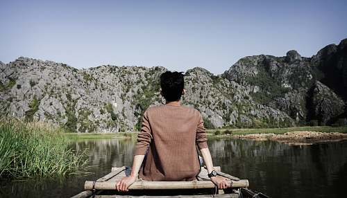 human man sitting on brown dock in front of gray rock formation person