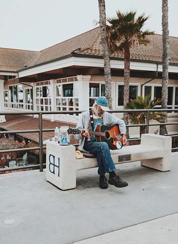 guitar man sitting on outdoor bench playing guitar during daytime musician
