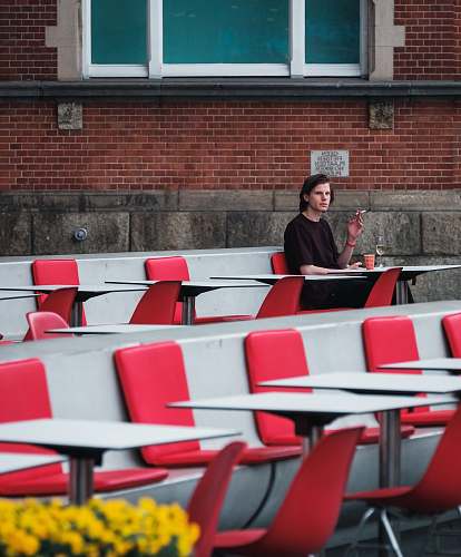 person man smoking cigarette while sitting on red chair brick