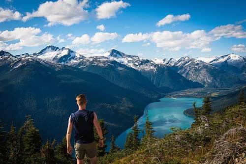 person man standing facing body of water and mountains during daytime human