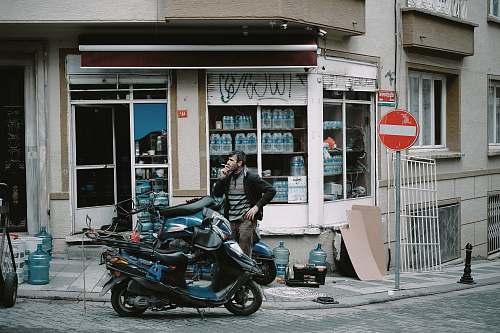 motorcycle man standing near black and blue motor scooter on road person