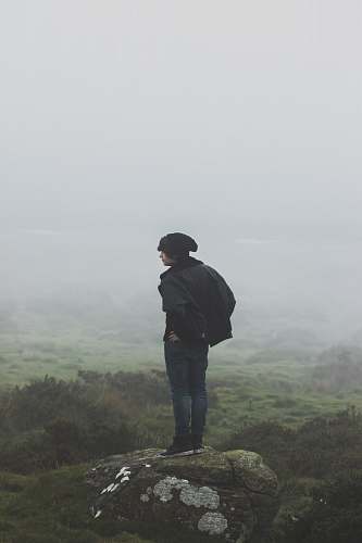 human man wearing black jacket standing on rock person