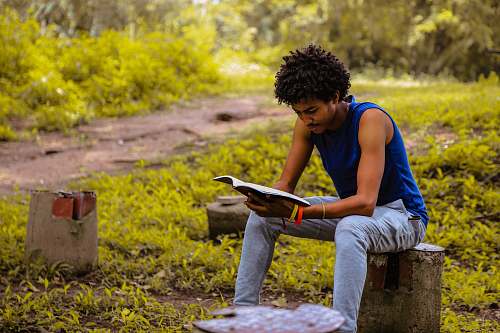 human man wearing blue shirt sitting on the bench reading book person