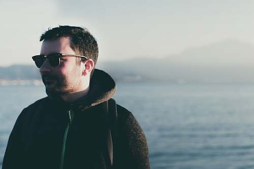 human man wearing eyeglasses standing near body of water person