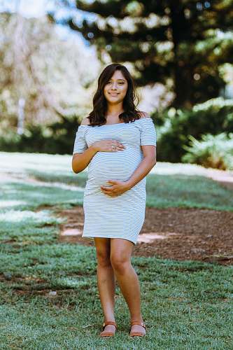 person maternity photography of woman in white and blue pinstripe off-shoulder mini dress standing on green grass human