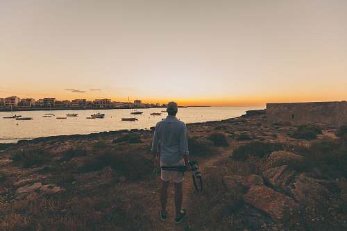 human person standing in open area overlooking body of water person