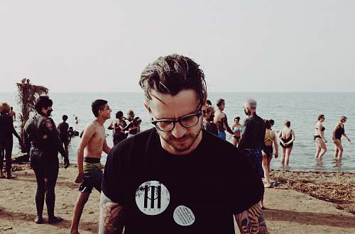 human photo of man wearing eyeglasses standing on beach during daytime person