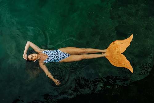 person photo of woman floating on body of water with mermaid tail flippers human