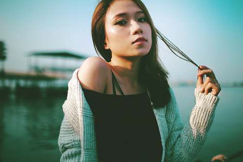 human selective focus photo of woman holding string of hair near body of water during daytime person