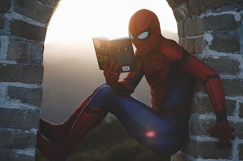 person Spider-Man leaning on concrete brick while reading book reading