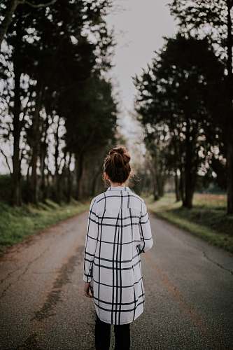 human tilt-shift lens photography of woman standing on gray road surrounded with trees person