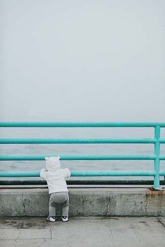 human toddler standing while resting arm on rail facing body of water person