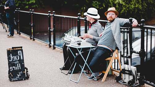 person two men sitting on bench while leaning on metal rail near poet hire signboard during daytime human