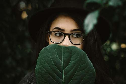 human woman covering her mouth with green leaf glasses