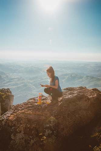 person woman holding smartphone while sitting beside orange bottle on top of rock formation human