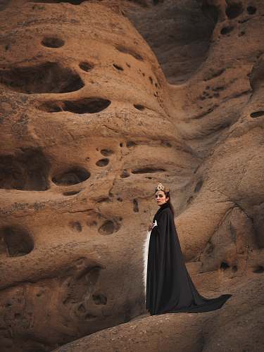 human woman in black cape standing on brown mountain person