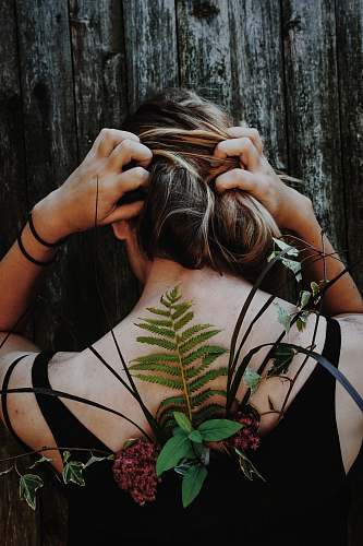 plant woman in black tank top with red petaled flower and assorted leaf on her back flora