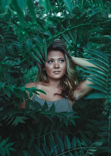 human woman in green sleeveless dress surrounded with green leaves at daytime person