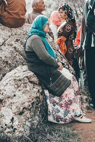 person woman in grey long-sleeved shirt and teal scarf sitting on rock during daytime human