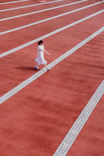 human woman in white dress walking on track and field person