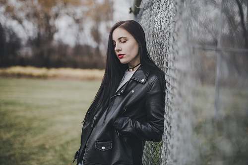 human woman leaning on cyclone fence with her right hand on her right jacket pocket person