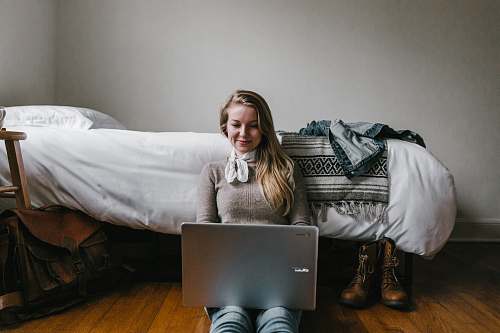 person woman sitting beside a bed while using a laptop human