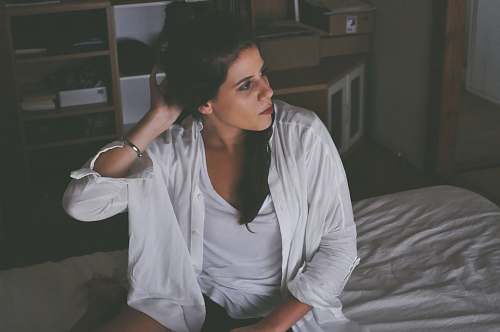 person woman sitting on bed touching her hair inside room white