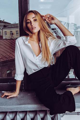 human woman sitting on gray pavement leaning on brown wall while holding her hair person
