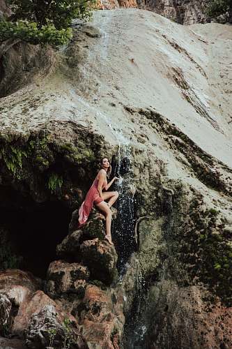 human woman sitting on rock under waterfalls person