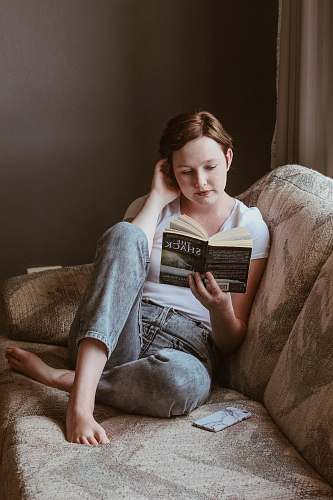 human woman sitting on sofa while reading book inside room reading